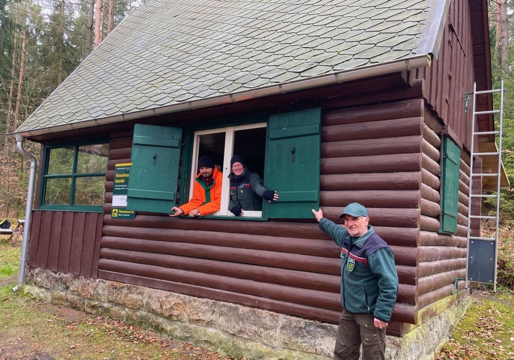 Die Haselmausbaude ist eine von fünf Forstbetriebshütten, die im Sommer anteilig durch die Forststeigwanderer genutzt werden können. Hüttenwart Wolfram Claus (r.), betreut die Hütten gemeinsam mit FöJ-ler Karl-Friedrich Neradt (l.). Maren Pussak (m.) trägt als Fachbereichsleiterin Naturerleben und Besuchermanagement die Verantwortung für das Gesamtprojekt des Trekkingroute „Forststeig Elbsandstein“.   Foto: U. Borrmeister