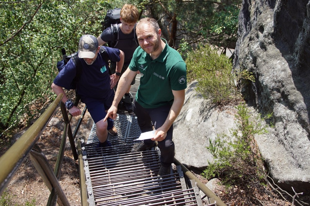 Martin Aulitzky (1. v. l.), Sachbearbeiter für Besuchereinrichtungen bei der Nationalpark- und Forstverwaltung Sächsische Schweiz, erklärt Wanderern aus Berlin die aufwendigen Maßnahmen für den Korrosionsschutz am Beispiel einer steilen Stiege entlang des Schrammsteingratwegs im Nationalpark Sächsische Schweiz.   Foto: K. Partzsch